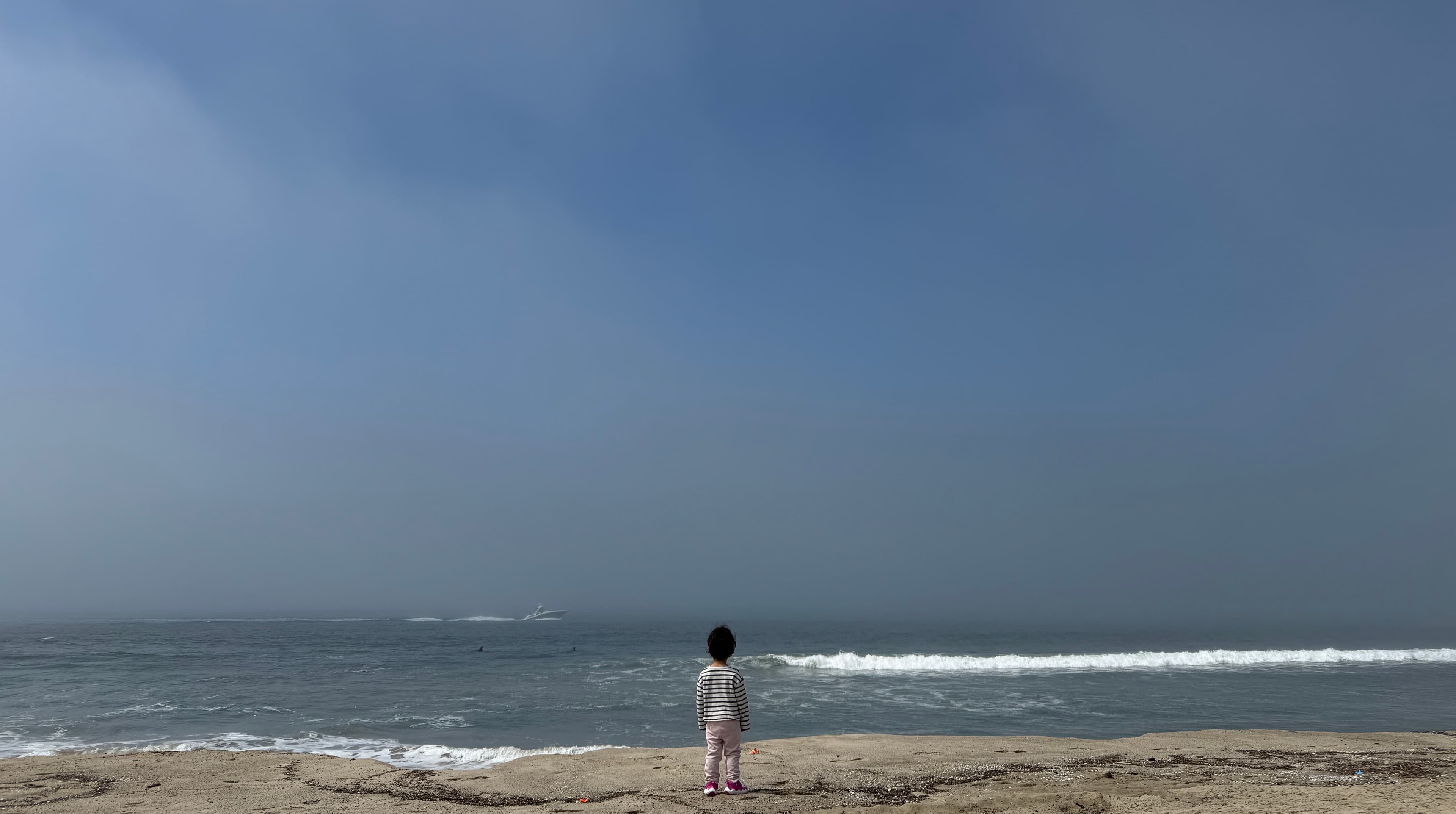 A child standing on the shore, looking out at the ocean